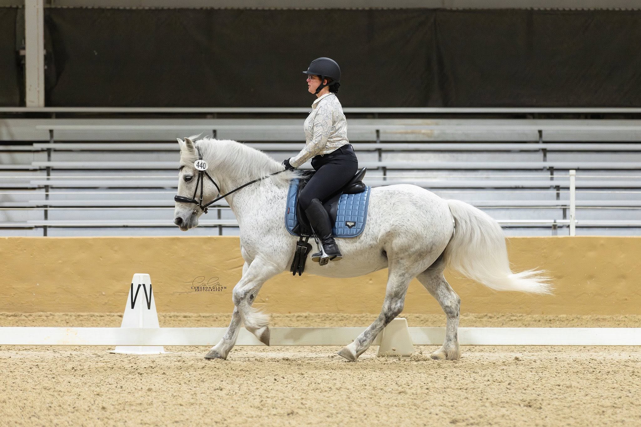A grey horse trotting under saddle at a show